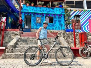 Vrouw in een Atitlan dorpje in Guatemala met een mountainbike. Ze staat voor een gekleurd huisje geposeerd.