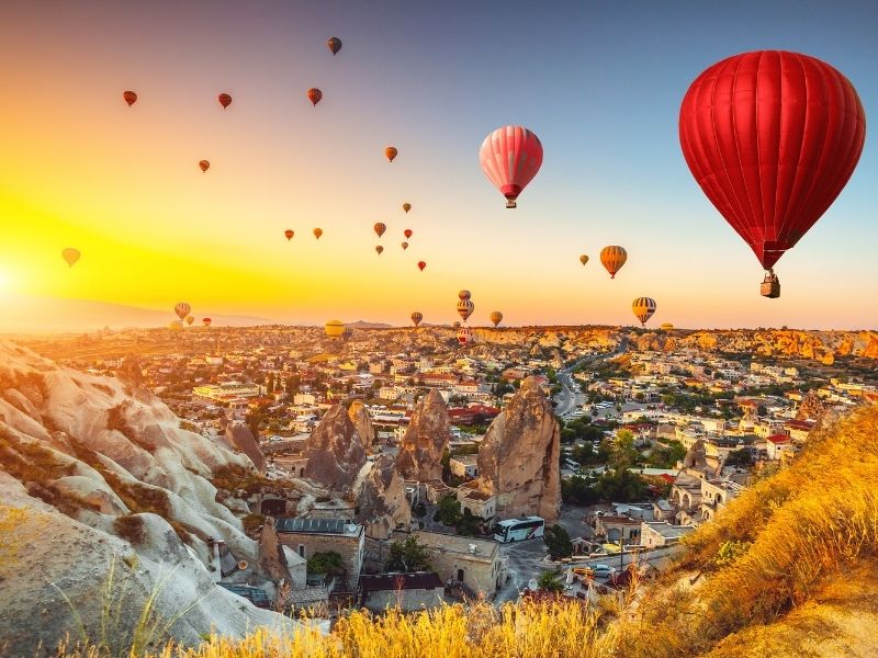 Kleurrijke luchtballonnen zweven bij zonsondergang boven het rotslandschap en de dorpen van Cappadocië in Turkije