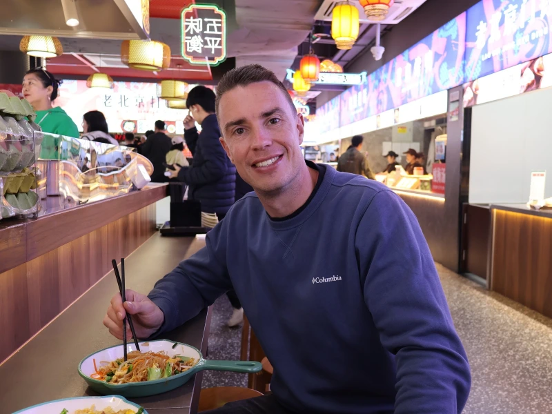 Man met blauwe trui aan in een restaurant in Hong Kong die een kom noedels zit te eten.