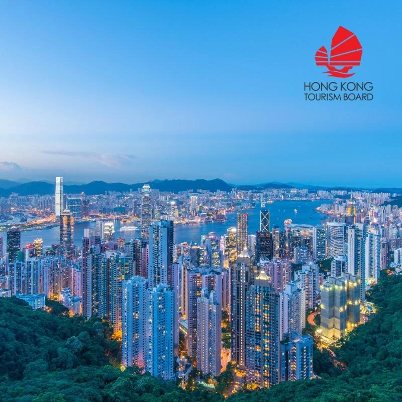 Uitzicht vanaf Victoria Peak in Hong Kong. Je ziet een zee van groene bomen op de voorgrond met daarachter de skyline van moderne gebouwen en flats op de achtergrond.