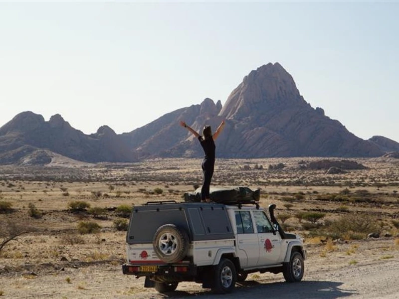 Reiziger staand op een jeep in een ruig woestijnlandschap in Namibië