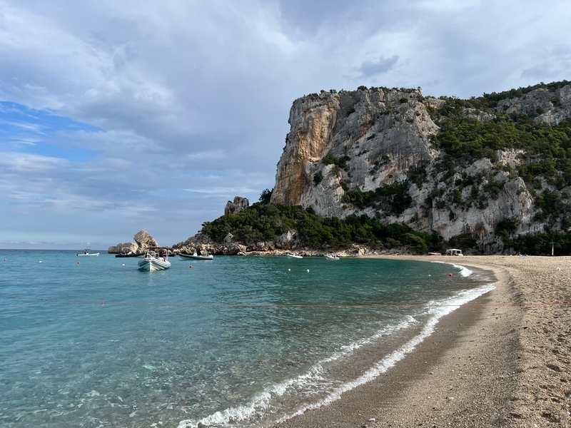 Italie-Sardinie-Supramonte-Mountains-Cala-Luna. Zandstrand met blauwe zee, waar bootjes in varen met bergen op de achtergrond