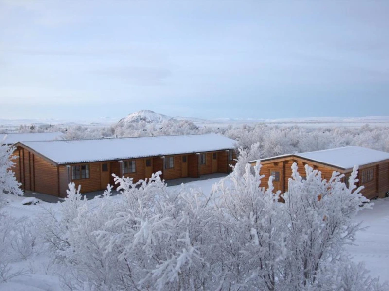 Houten huisjes staan tussen besneeuwde bomen in een winterlandschap.