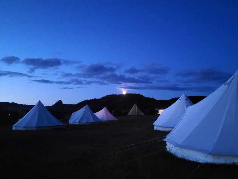 Witte tenten op een veld in de schemering met de maan boven de heuvels.