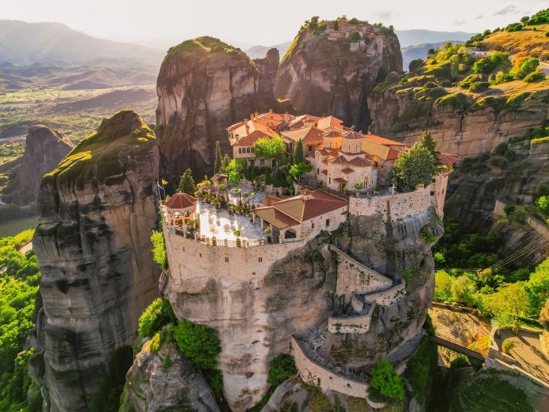 Klooster van Meteora in Griekenland, spectaculair gebouwd op een hoge rotsformatie, omringd door groene valleien en imposante bergen.