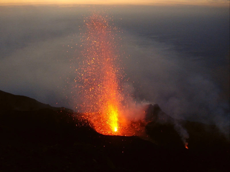 Uitbarstende vulkaan spuit lava en vonken de lucht in tijdens zonsondergang.