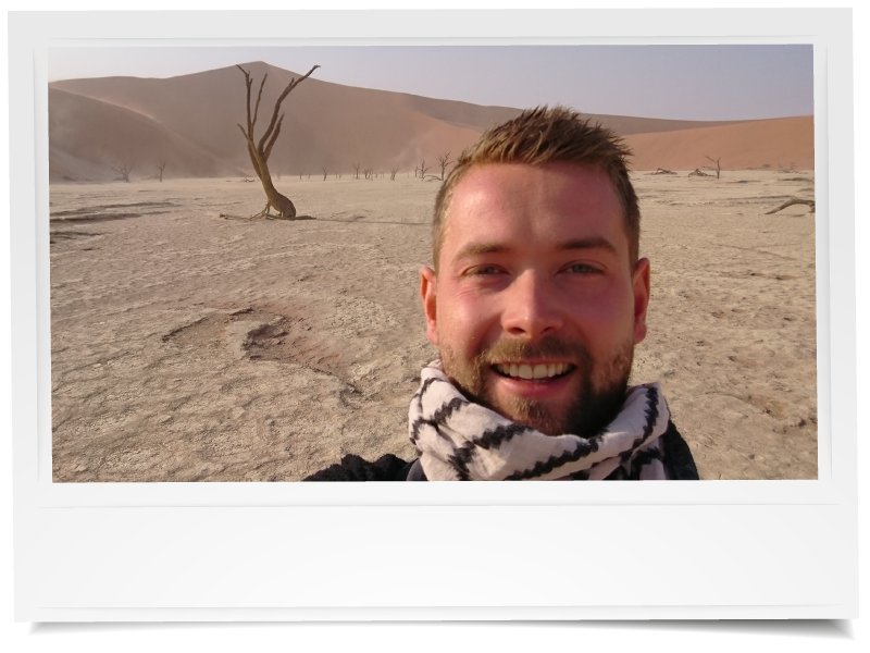 Selfie van een man in de woestijn van Deadvlei in Namibië, met achter hem de witte kleivlakte, dorre bomen en hoge oranje zandduinen.