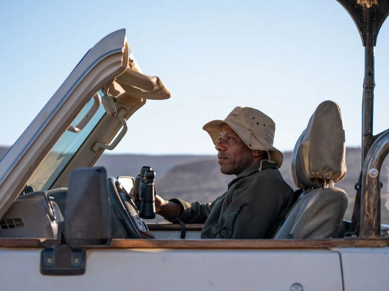 Lokale gids zit in een jeep met een verrekijker in Namibië