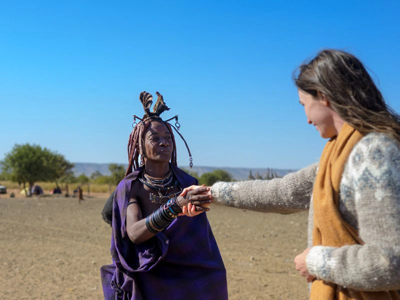 Vrouw van de Himba-stam en reiziger ontmoeten elkaar en schudden elkaar de hand.