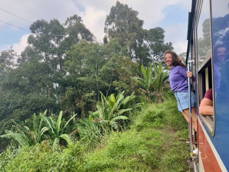 Reiziger hangt uit rijdende trein in Sri Lanka in een groene omgeving