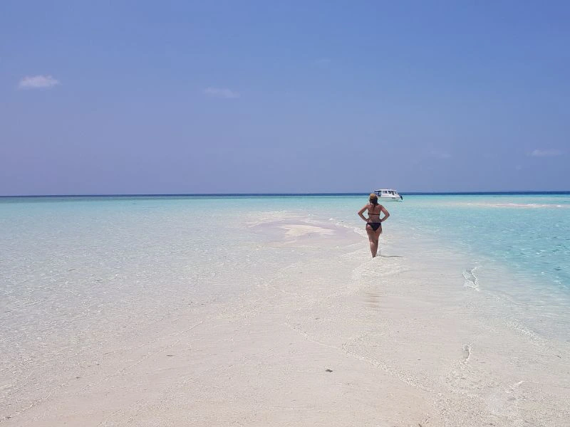 Reiziger wandelt op het witte zand en in het ondiepe kristalheldere water van de Malediven