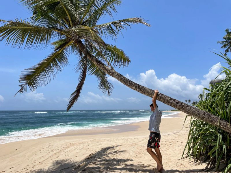 Reiziger hangt aan een palmboom op het strand.