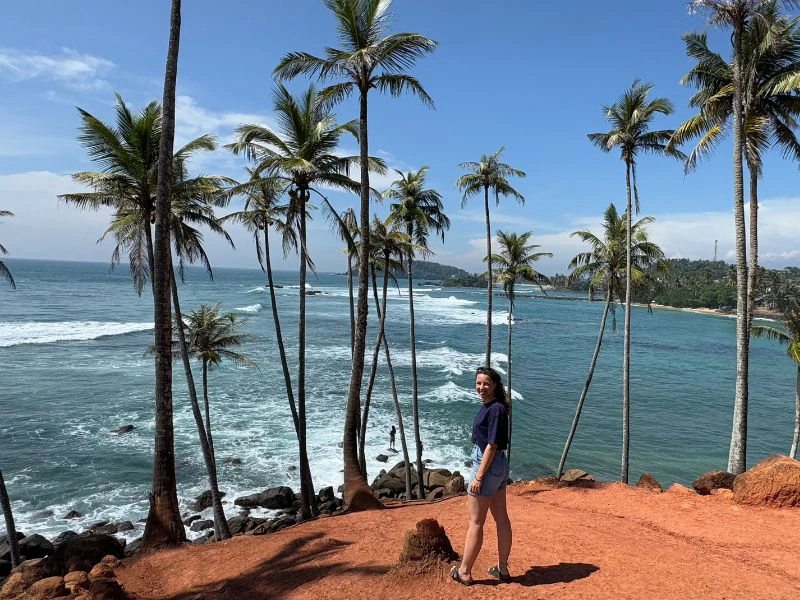 Vrouw staat tussen de palmen met uitzicht op zee.