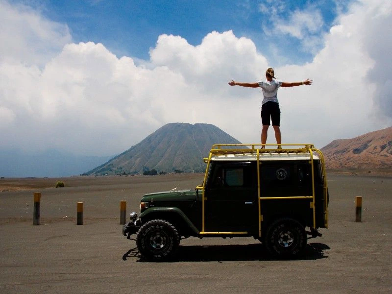 Vrouwelijke reiziger staand op een stoere 4x4 op het maanlandschap van de Bromo