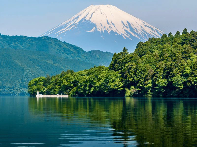 Lake Ashi in Hakone, Japan, met groene beboste oevers en de met sneeuw bedekte top van Mount Fuji op de achtergrond.