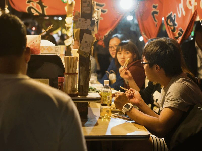 Mensen zitten aan een bar van een yatai-straatkraam in Fukuoka, Japan, en eten met stokjes.