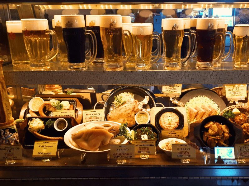 Etalage van een Japans restaurant met verschillende gerechten en grote glazen bier op display.