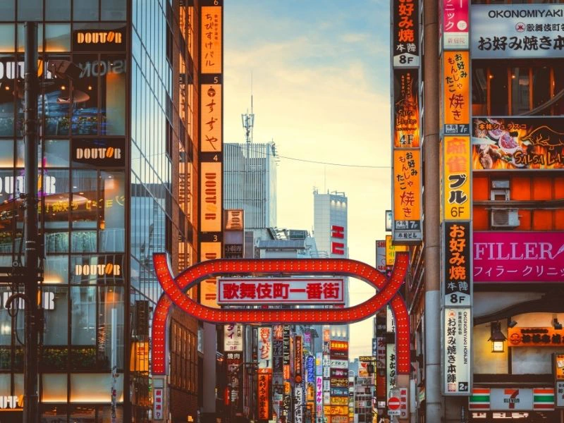 Verlichte straat met kleurrijke neonreclames en hoogbouw in Shinjuku, Tokyo, Japan, bij zonsondergang.