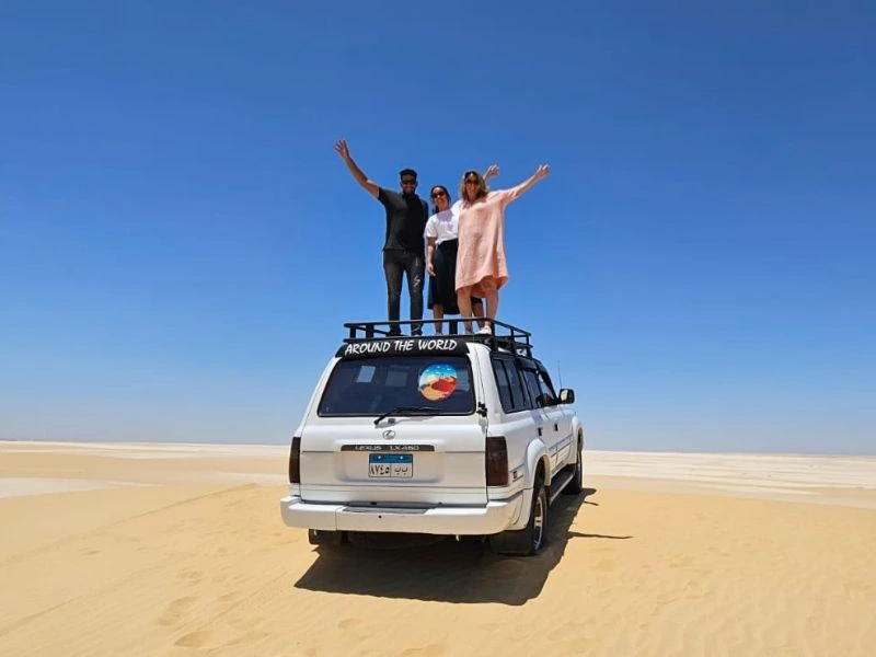 Drie mensen staan op een auto in de woestijn van Egypte
