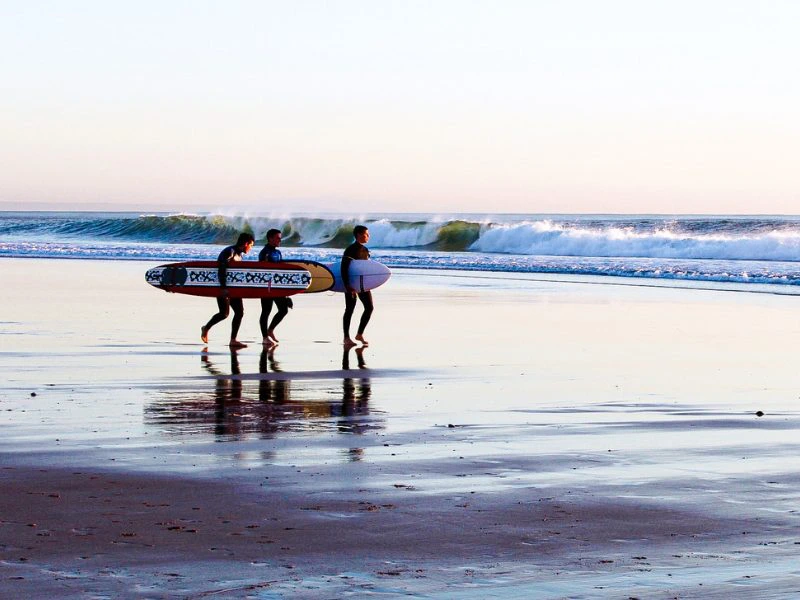 Drie surfers met boards op het strand in Portugal