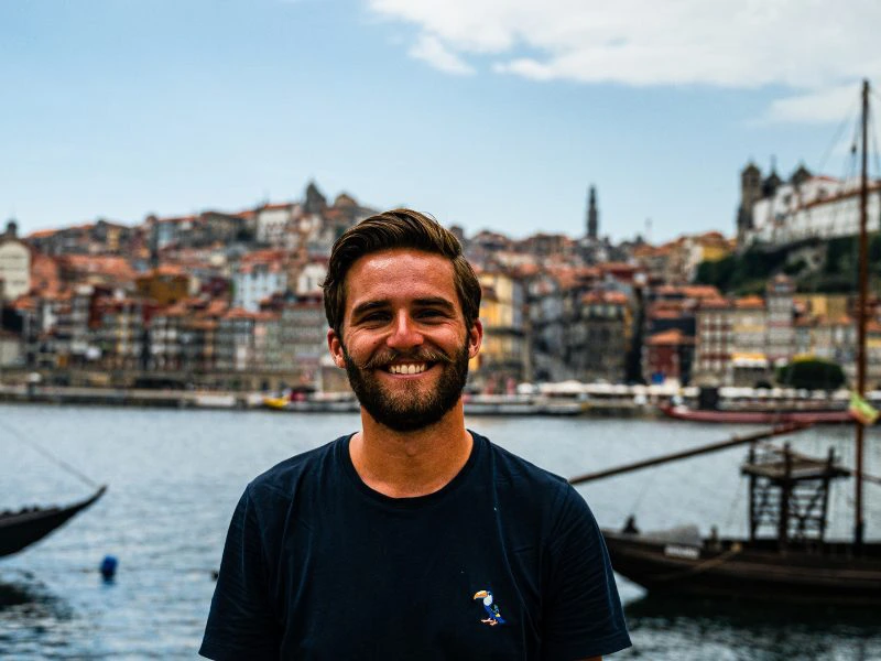 Lachende man staat aan de waterkant met uitzicht op kleurrijke historische huizen en boten op de rivier, waarschijnlijk in Porto, Portugal