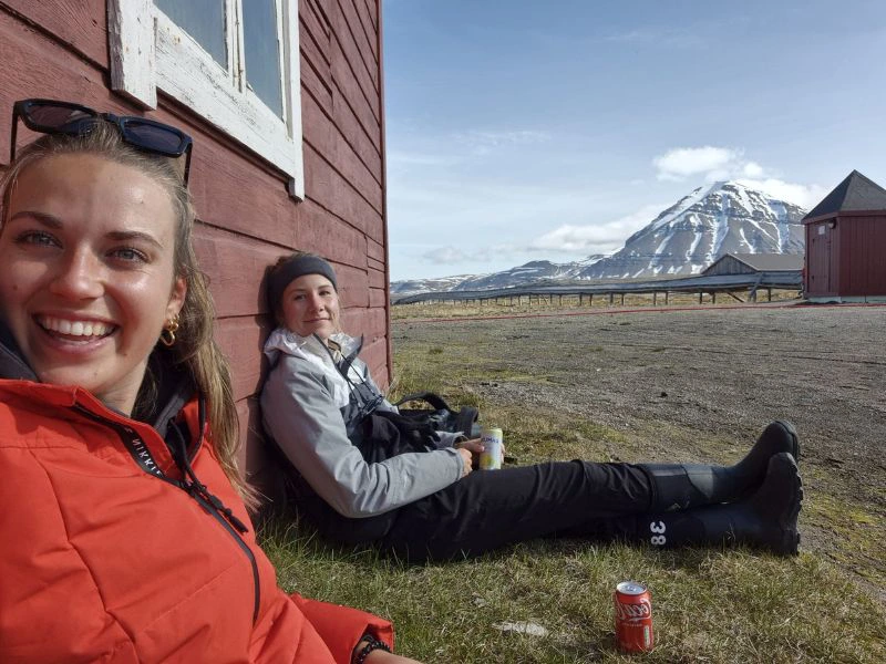 Reisexperts Bibi en Michelle rusten tegen een houten huisje tijdens hun reis door Noorwegen