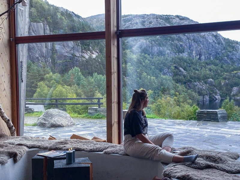 Vrouw zit voor het raam te genieten van het prachtige uitzicht: bergen op de achtergrond en een langsstromende rivier.