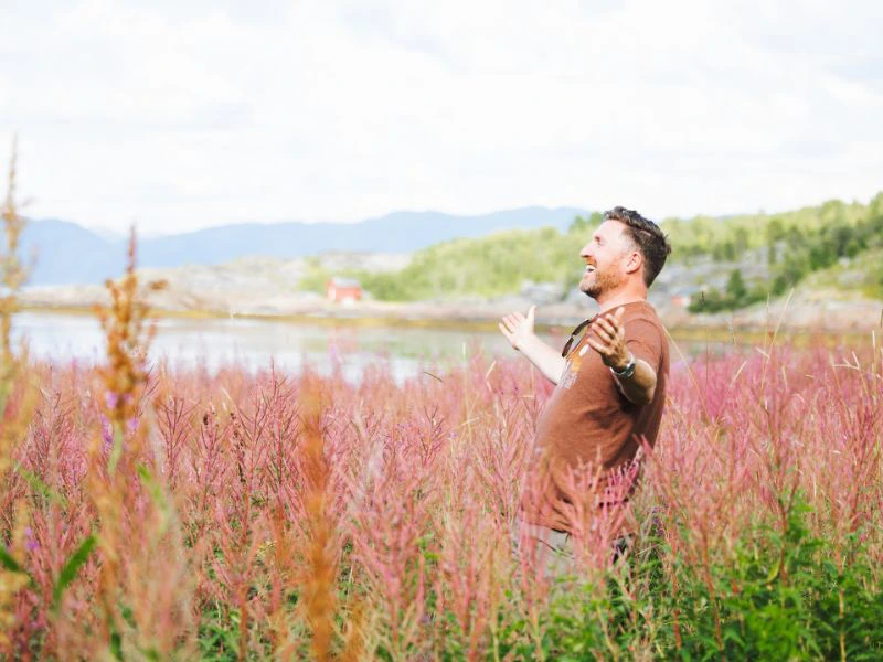 Man staat lachend in het midden van de natuur met een lentezon op zijn gezicht.