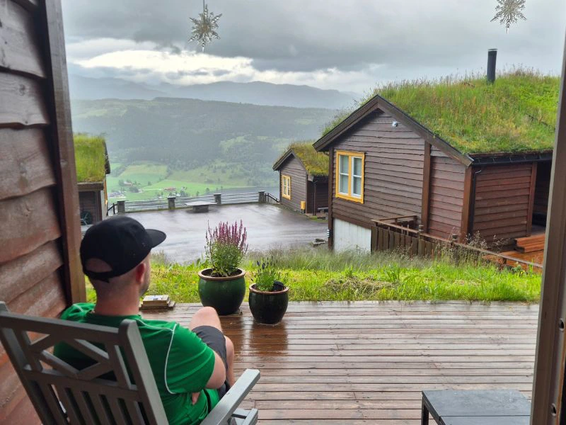 Man zit op het terras van zijn houten vakantiehuisje en geniet van het uitzicht.