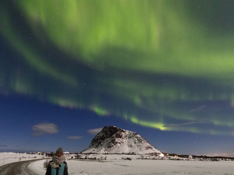 Reiziger staat in op een sneeuwvlakte in Noorwegen met het Noorderlicht.