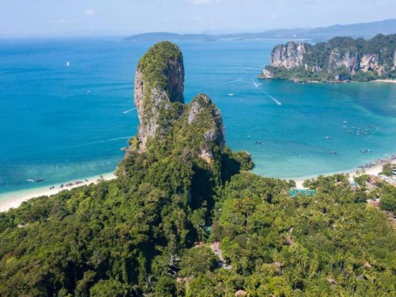 Luchtfoto van het tropische Railay Beach met steile kalkstenen rotsformaties, groene jungle en turquoise zee, omringd door witte zandstranden en bootjes op het water.