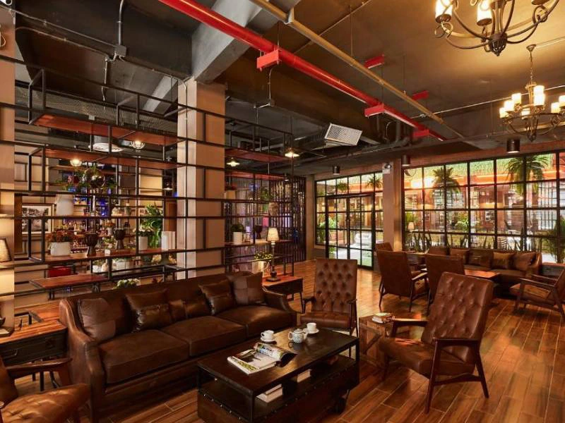 Een sfeervolle lounge met leren banken en stoelen, warme verlichting en een industriële look door het open plafond en metalen rekken.