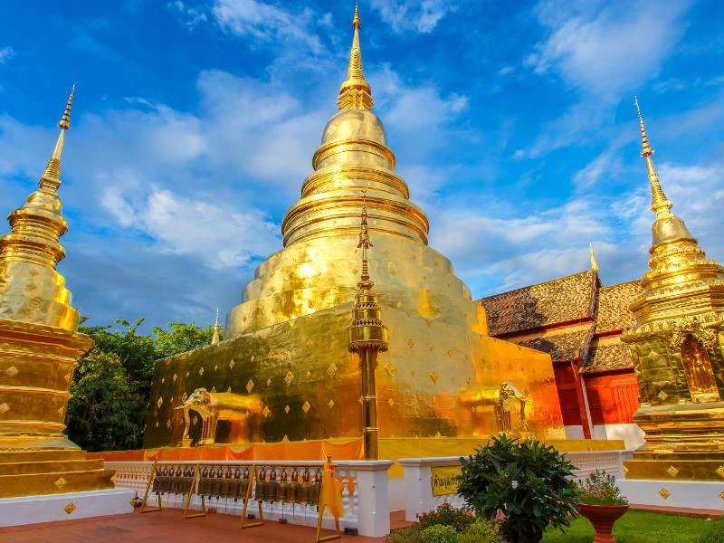 Gouden tempels in Chiang Mai glanzen in het zonlicht onder een deels bewolkte blauwe lucht, met kleurrijke details en een rustige sfeer op het tempelplein.
