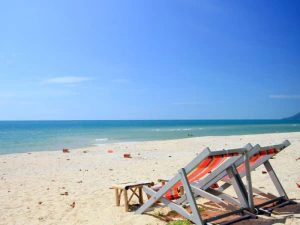 twee strandstoelen op een verlaten goudgeel strand met een blauwe zee en blauwe lucht in de achtergrond