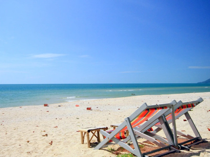 twee strandstoelen op een verlaten goudgeel strand met een blauwe zee en blauwe lucht in de achtergrond