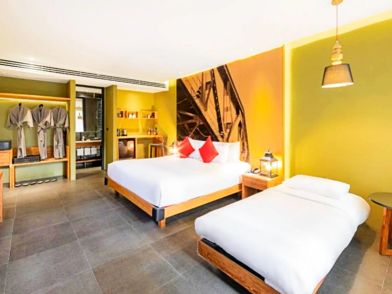 Hotelkamer met een tweepersoonsbed en een eenpersoonsbed, groene muren, open kledingkast met badjassen en industriële muurdecoratie.