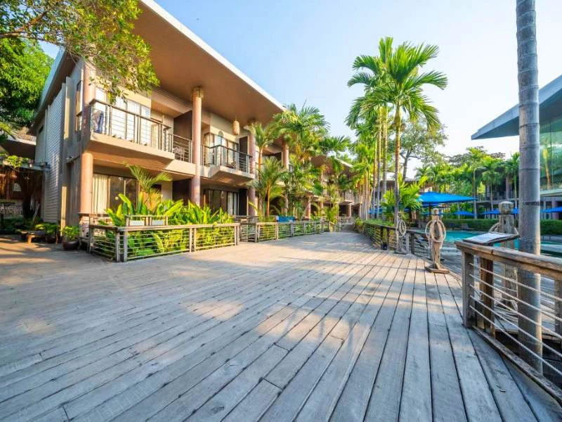 Luxe resort met moderne kamers en balkons, omgeven door palmbomen en een houten promenade.