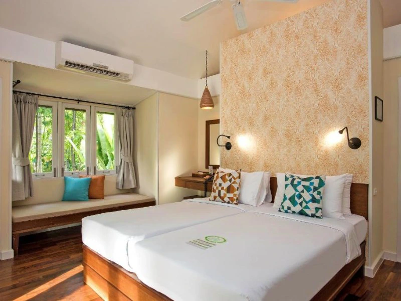 Lichte en sfeervolle hotelkamer met twee eenpersoonsbedden, kleurrijke kussens en uitzicht op tropisch groen.