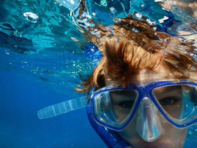 Kind met snorkelmasker onder water, deels boven wateroppervlak.
