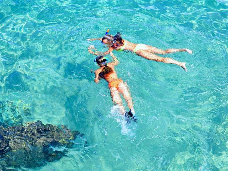 Twee personen snorkelen in helderblauw water boven een rotsformatie.