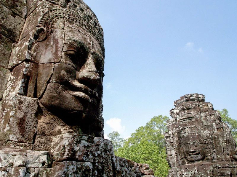 Twee stenen torens van de Bayon-tempel in Cambodja, met gigantische gebeeldhouwde gezichten tussen het groen van de jungle en de heldere blauwe lucht.