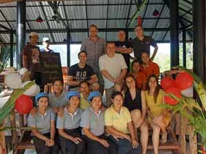 Groepsfoto van medewerkers in en voor een openluchtgebouw, met ballonnen ter versiering.