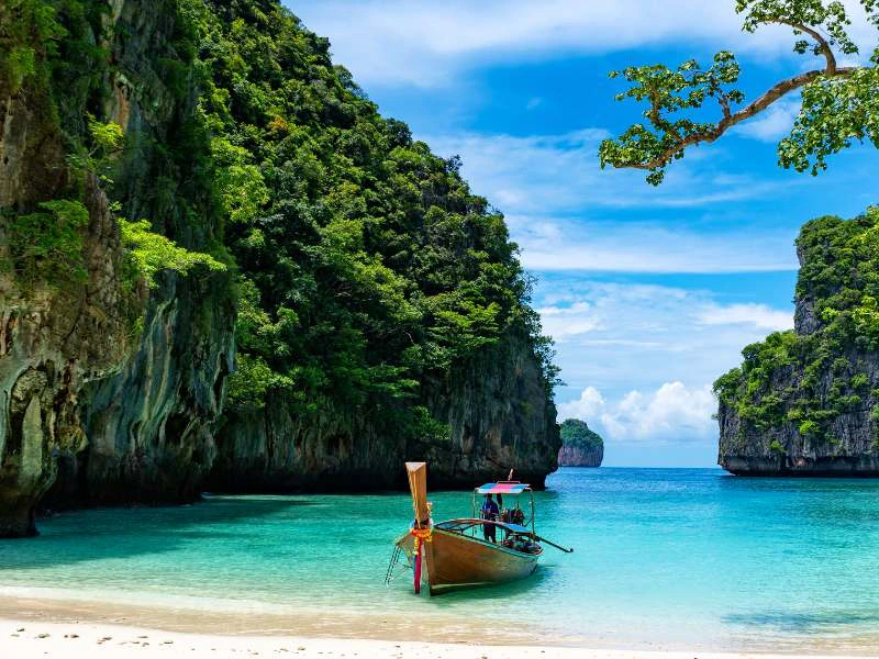 Traditionele longtailboot dobbert in turquoise water tussen groene kalksteenrotsen en tropisch strand.