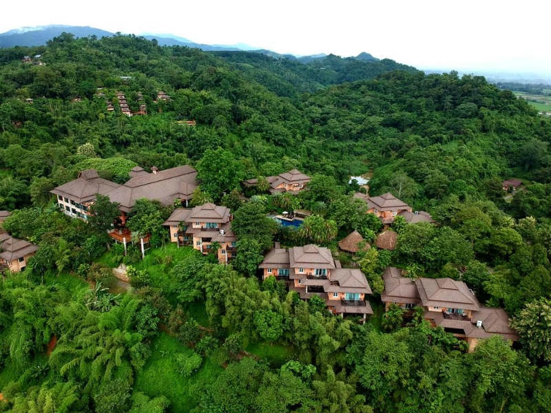 Luchtfoto van beboste bergen met verspreid gelegen huizen, waarvan vooral de daken door het bladerdek zichtbaar zijn.