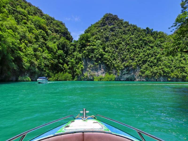 Uitzicht vanaf een boot op helderblauw water en groene, steile rotsen onder een stralend blauwe lucht.