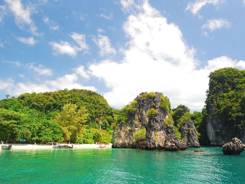 Groene rotsen en helder turquoise water bij een tropisch strand met longtailboten.