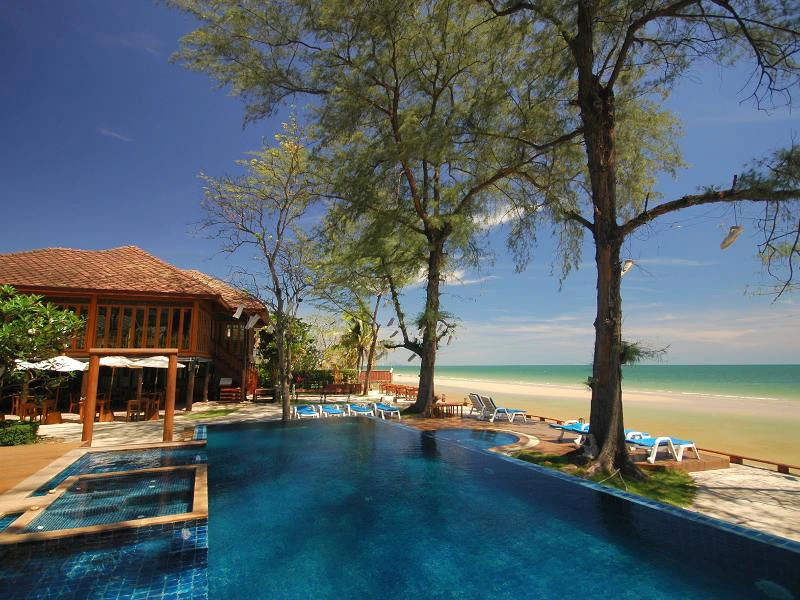 Zwembad bij tropisch strandresort met ligstoelen, palmbomen en uitzicht op zee.