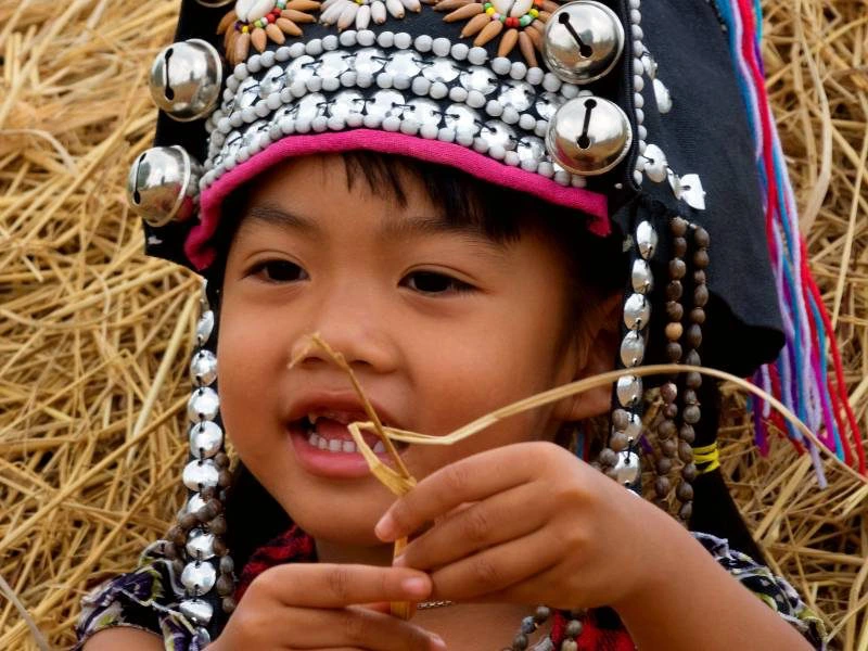 Gezicht van een kindje met een traditionele hoofd tooien zwart haar, staand voor een hooi baal