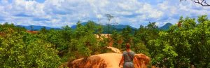 Vrouw wandelt over een smal zandpad langs de rotsen van Pai Canyon in Thailand, met uitzicht op groene jungle en bergen in de verte.