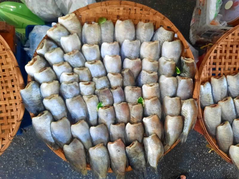 Mand met vissen, rechtopstaand en netjes gerangschikt, uitgestald op de grond van een markt.